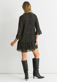 Black polka dot dress with a ruffled hem, sheer fabric, and three-quarter bell sleeves, paired with knee-high black heeled boots.