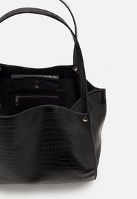 Mustat krokotiilikuosiset laukut, joissa on kaksi kahvaa, avoin yläosa ja sisätasku, jossa on vetoketju. Sileä pinta, jämäkkä muoto.