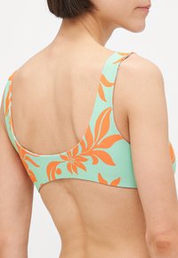 Haut de bikini fleuri avec une base vert menthe et des motifs de feuilles orange, larges bretelles et une texture lisse et extensible.