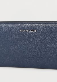 Πορτοφόλι από δερματίνη σε ναυτικό μπλε με υφή, διακοσμημένο με ασημένια επωνυμία «MICHAEL KORS». Κλείσιμο με φερμουάρ, με ομαλές άκρες και μινιμαλιστικό σχεδιασμό.
