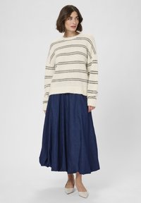 Krém színű pulóver fekete csíkokkal, kerek nyakkivágással és hosszú ujjakkal, sötétkék, lágyan omló szoknyával párosítva. A szoknya texturált felületű.