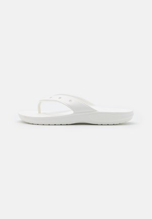 Hvid slip-on sandal med tåspange og ventilationshuller, flad sål med tekstureret greb, vist i sidevisning på ensfarvet baggrund.
