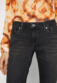Svarta jeans med smal passform, utrustade med fem fickor, silverdetaljer och kontrasterande söm. Kombinerat med en blus i orange batik.