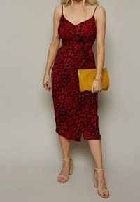 Rotes Kleid mit Leopardenmuster, Spaghettiträgern, knielang, figurbetont, weiche Textur. Kombiniert mit einer gelben Clutch und beigen Sandalen mit Blockabsatz.