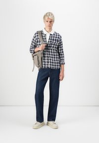 Camisa a cuadros en azul marino y blanco, mezcla de algodón. Jeans rectos en azul oscuro. Bolsa gris con cremalleras. Zapatillas blancas con cuello y crema.