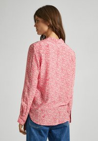 Blusa a maniche lunghe rosa con motivo floreale bianco, con orlo arrotondato, dettagli con bottoni sui polsini e vestibilità rilassata.