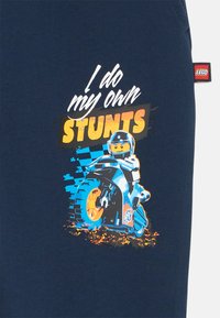 Navyblaues T-Shirt mit einem Grafikmotiv eines LEGO-Charakters auf einem Motorrad, umgeben von dem Text "Ich mache meine eigenen STUNTs" in leuchtenden Farben.