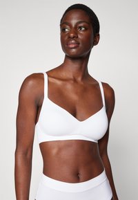White wireless bra with a smooth finish, adjustable straps, and a deep V-neckline, paired with matching white briefs.