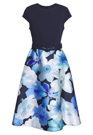 Robe bleu marine à manches casquette, corsage ajusté, ceinture noire et jupe évasée avec grand imprimé floral blanc et bleu.