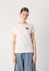 Cream-colored cotton t-shirt with short sleeves, featuring a black embroidered design on the left chest. Casual fit.