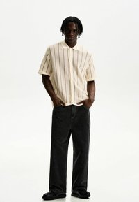 Short-sleeve, beige knit polo shirt with vertical stripes, paired with loose-fitting black jeans and black shoes. Smooth texture and casual design.