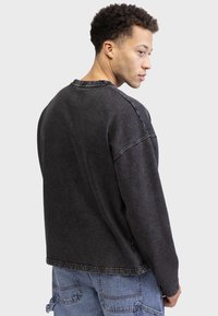 Sweatshirt oversize gris foncé avec un col rond, des épaules tombantes et des détails de couture visibles. Texture douce et design épuré.