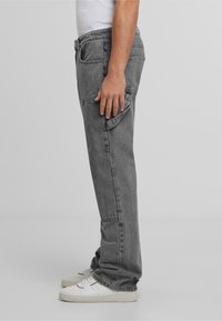 Graue Denim-Cargo-Hosen mit Seitentaschen, geradem Bein Design und leicht verblasster Textur, getragen mit weißen Sneakern.