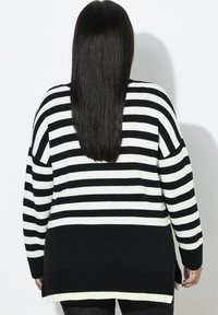 Maglione a righe bianche e nere in maglia, con una vestibilità comoda, polsini a coste e un orlo posteriore più lungo. Presenta ampie righe orizzontali.
