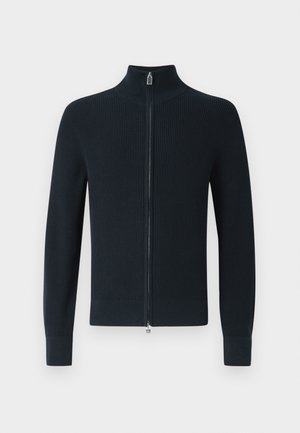 Maglione blu scuro a coste con cerniera, colletto alto, maniche lunghe e dettaglio della cerniera argentata sul davanti. Tessuto morbido a maglia.