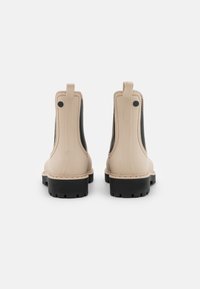 Botines beige hasta el tobillo con paneles laterales elásticos, suelas de goma negra, lengüetas y costuras a lo largo del borde de la suela.