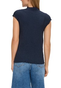 Donkerblauw T-shirt met korte mouwen, voorzien van een gestructureerd wafelpatroon, met een gekartelde halslijn en een relaxte pasvorm. G gedragen met lichtblauwe jeans.