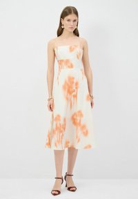 Hihaton midi-mekko kermanvärissä, jossa on oranssi abstrakti kukkakuosi, istuva yläosa ja levenevä hame; yhdistetty ruskeisiin nilkkapietoihin.