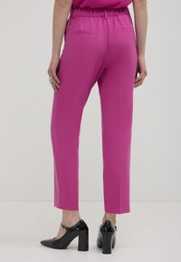 Pantaloni aderenti a vita alta in tessuto rosa vivace, con una cintura elastica, tasche posteriori e abbinati a scarpe con tacco alto nere.