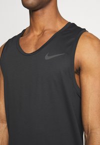 Débardeur noir Nike sans manches avec une texture lisse, un col arrondi et un logo discret sur le côté supérieur gauche.