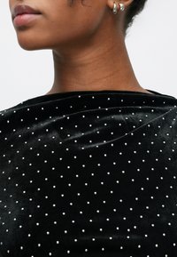 Material din catifea neagră cu o textură netedă, împodobit cu mici ornamente argintii aranjate într-un model punctat.