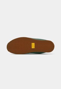 Semelle de chaussure avec un motif de tissage en zigzag brun et un logo Nike rectangulaire jaune près du centre.