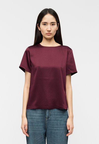 T-shirt bordeaux à manches courtes en tissu lisse, avec un col bateau et une coupe décontractée. Associé à un pantalon en denim bleu taille haute.