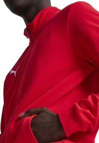 Rote Zip-Jacke aus weichem Stoff mit einem taillierten Kragen und gerippten Bündchen. Verfügt über ein weißes Logo auf der linken Brust und seitliche Taschen.