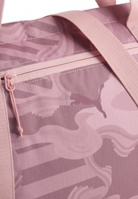 Sac de voyage rose à motifs avec une fermeture éclair visible, des sangles réglables et un logo Puma discret. Confectionné en tissu robuste et texturé.
