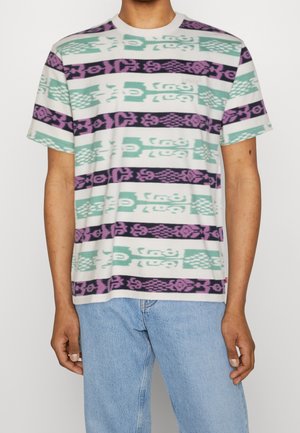 Kortærmet T-shirt har et mønstret design med skiftende striber i grønblå, lilla og sort på en lys baggrund.