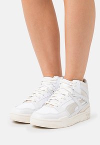 White high-top sneakers with a mix of smooth leather and soft suede. Features lace-up design and perforated toe for breathability.