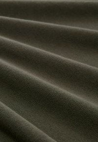 Olijfgroen katoenen stof met een zachte textuur, voorzien van diagonale plooien die diepte en natuurlijke vloei tonen. Gladde oppervlakte met minimale glans.