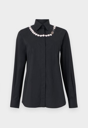 Crna košulja dugih rukava s gumbima, šiljastim ovratnikom i ukrasnim bijelim lančićem od bisera te zlatnim kopčanjem duž izreza.
