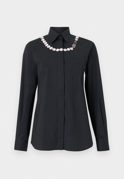 Μαύρο πουκάμισο με μακριά μανίκια και κουμπιά, με μυτερό γιακά που διαθέτει διακοσμητική λευκή αλυσίδα από πέρλες και λεπτομέρεια με χρυσή αγκράφα κατά μήκος του λαιμού.