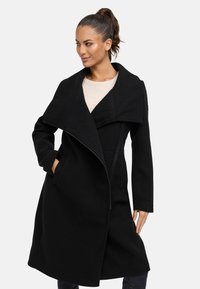 Manteau en laine noire avec un large col, fermeture éclair frontale asymétrique, poches latérales et coupe ajustée. Texture lisse et design moderne.