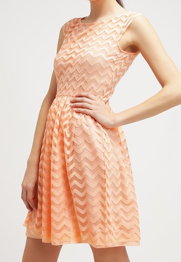 Robe sans manches de couleur pêche avec un motif en zigzag, corsage ajusté et jupe évasée. Fabriquée en tissu texturé avec un léger éclat.