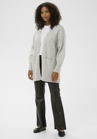 Jasnoszary sweter z dzianiny z prążkowanymi mankietami i dołem, z dwoma przednimi kieszeniami. Noszony na białą koszulę i zestawiony z czarnymi skórzanymi spodniami.