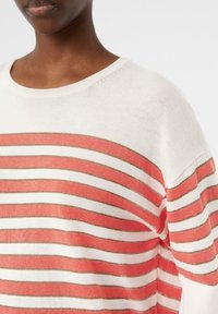 Gestreifter Strickpullover mit korallenroten, weißen und goldenen horizontalen Streifen. Der Stoff hat eine weiche Textur und einen lockeren Schnitt, mit einem weiten Ausschnitt.