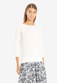 Weiße Langarmbluse mit einem Bootsausschnitt, weichem Stoff und eng anliegenden Bündchen, kombiniert mit einem gemusterten Rock in Blau und Weiß.