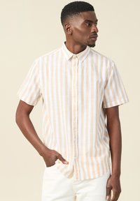 Camicia a maniche corte con bottoni in righe beige e bianche, dotata di colletto classico, texture liscia e tessuto leggero.