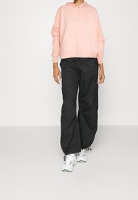 Felpa rosa con un motivo testurizzato, tasca frontale e cordini; abbinata a pantaloni cargo neri larghi e sneaker bianche.