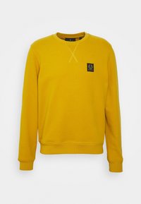 Gul sweatshirt med rund hals, ribbade ärmslut och nederkant. Har ett litet svart logotyppatch på bröstet och kontrasterande sömmar.