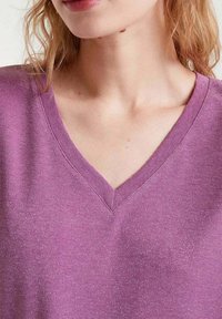 Top de cuello en V en suave tela de lavanda texturizada con un ligero brillo. Presenta un escote limpio y un corte relajado.