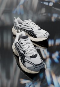 Chaussures de sport noires et blanches avec une tige en mesh, des accents texturés et une semelle rembourrée. Comprend des lacets et un logo sur le côté.