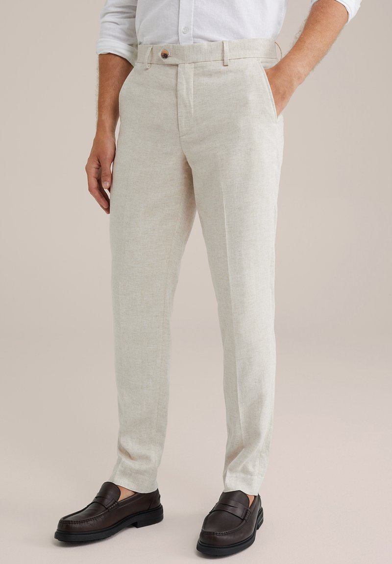 Beige len nadrág, testhez simuló szabással, gombos záródással és ferde zsebekkel. Sötét bőrcipőkkel egészítve.