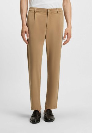 Beige trousers with a tailored fit, featuring a flat front, belt loops, and two side pockets. Worn with black loafers.