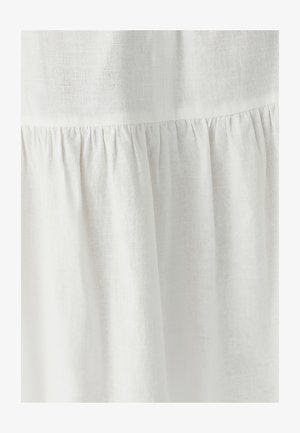 Vestido blanco de lino con una superficie texturizada y detalles fruncidos en el dobladillo, creando una apariencia fluida.