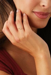 Gul zigzag ring bæres på pegefingeren, der fremhæver et minimalistisk design med en glat overflade og en poleret finish.