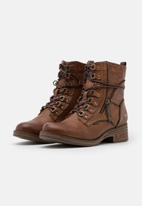 Botine din piele maro cu design cu șireturi, fermoare decorative, modele embossate și toc mic pătrat. Dispune de ochiuri metalice și accesorii.