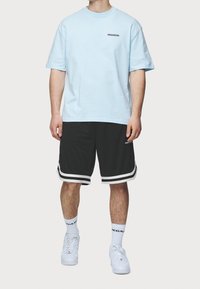 Ljusblå bomullst-shirt med svart "PEGADOR"-logotyp, kombinerad med svarta sportshorts med vita ränder och detaljer. Vita sneakers.